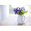 Bouquet of wild flowers in white vase on rustic wooden table near window with copy space, natural light