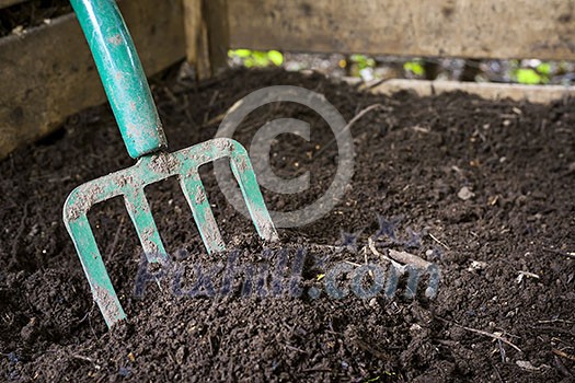 Garden fork turning black composted soil in wooden compost bin Garden fork turning black composted soil in wooden compost bin