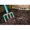 Garden fork turning black composted soil in wooden compost bin