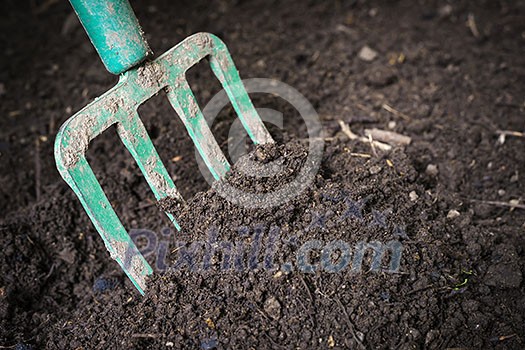 Garden fork turning  black composted soil in compost bin ready for gardening, close up.
