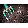 Garden fork turning  black composted soil in compost bin ready for gardening, close up.