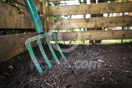 Garden fork turning black composted soil in wooden compost bin