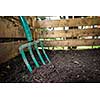 Garden fork turning black composted soil in wooden compost bin