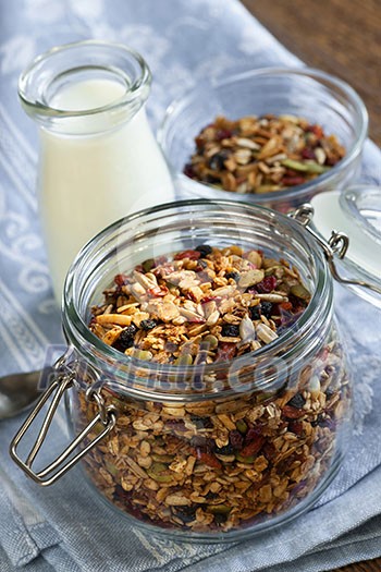 Homemade granola in open glass jar and milk or yogurt on table with linens Homemade granola in open glass jar and milk or yogurt on table with linens