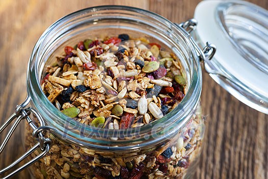 Homemade granola in open glass jar on rustic wooden background Homemade granola in open glass jar on rustic wooden background