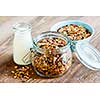 Homemade granola in open glass jar and milk or yogurt  on rustic wooden background