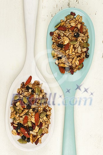 Homemade granola with various seeds and berries in two wooden spoons shot from above on wood background Homemade granola with various seeds and berries in two wooden spoons shot from above on wood background