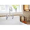 Rustic white porcelain kitchen sink with curved faucet and tile backsplash under large window