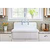 Kitchen interior with large rustic white porcelain sink and granite stone countertop under sunny window