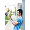 Young asian man smiling and looking at smart phone on city sidewalk