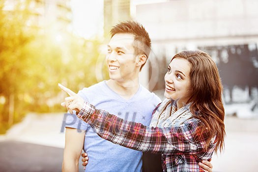 Romantic interracial young couple standing together pointing outside in sunset light with intentional lens flare Romantic interracial young couple standing together pointing outside in sunset light with intentional lens flare