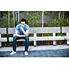 Concerned young asian man sitting on park bench with copy space