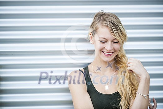 Candid portrait of young blonde woman looking down against corrugated metal background and copy space Candid portrait of young blonde woman looking down against corrugated metal background and copy space