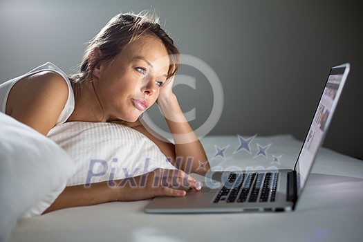 Pretty, young woman using her laptop computer in bed (color toned image; shallow DOF) Pretty, young woman using her laptop computer in bed (color toned image; shallow DOF)