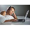 Pretty, young woman using her laptop computer in bed (color toned image; shallow DOF)