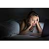 Pretty young woman watching something awful/sad on her laptop in bed at night in a dark bedroom (shallow DOF; color toned image)