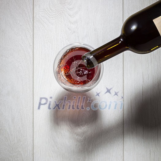 Red wine pouring into glass from bottle on white wooden table. Top view Red wine pouring into glass from bottle on white wooden table. Top view