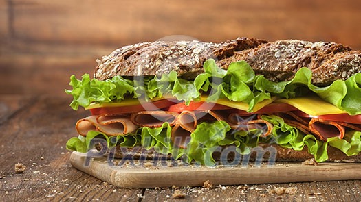 Sandwich on the wooden table with slices of fresh tomatoes, ham, cheese and lettuce Sandwich on the wooden table with slices of fresh tomatoes, ham, cheese and lettuce