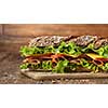 Sandwich on the wooden table with slices of fresh tomatoes, ham, cheese and lettuce