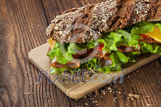 Sandwich on the wooden table with slices of fresh tomatoes, ham, cheese and lettuce Sandwich on the wooden table with slices of fresh tomatoes, ham, cheese and lettuce