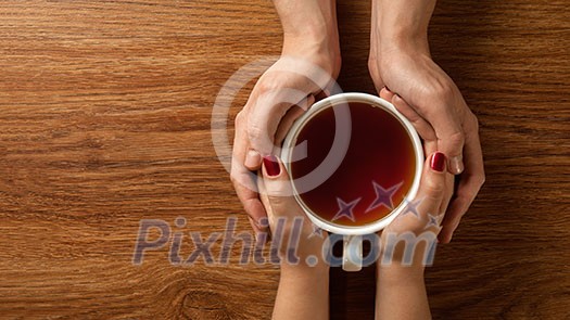 Womans and mens hands holding hot cup of tea on wooden table. Header for website Womans and mens hands holding hot cup of tea on wooden table. Header for website