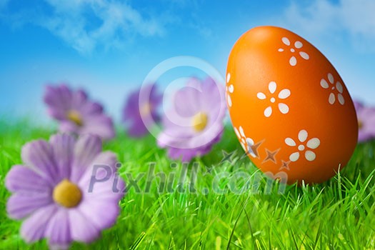 Orange easter egg in the grass against blue sky Orange easter egg in the grass against blue sky