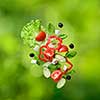 flying salad on natural green background - red tomatoes, pepper, cheese, basil, cucumber and olives