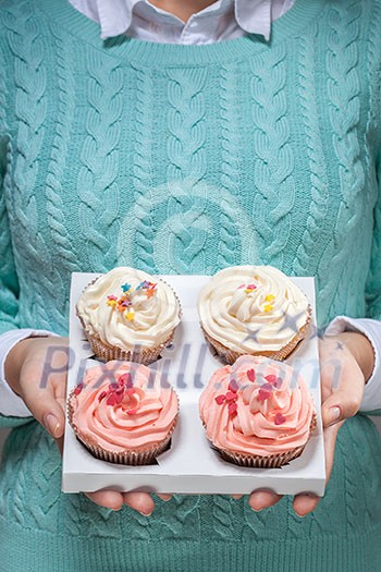 young woman holding a box of colorful cupcakes decorated with hearts and stars young woman holding a box of colorful cupcakes decorated with hearts and stars