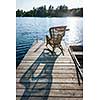 Wicker rocking chair on wooden dock in summer at small lake casting long shadow