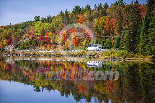 Tour bus driving though fall forest with colorful autumn leaves reflecting in lake. Highway 60 at Lake of Two Rivers, Algonquin Park, Ontario, Canada. Tour bus driving though fall forest with colorful autumn leaves reflecting in lake. Highway 60 at Lake of Two Rivers, Algonquin Park, Ontario, Canada.