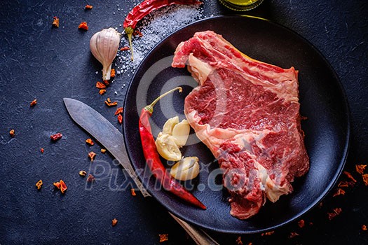 Raw meat steak entrecote on the plate with spice on the dark table Raw meat steak entrecote on the plate with spice on the dark table