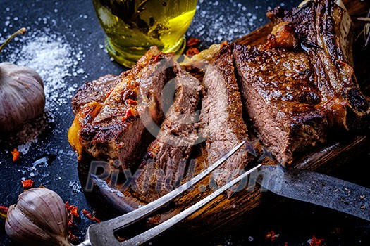 Grilled steak sliced on a cutting board. Entrecote with garlic and chilli on a dark background. Grilled steak sliced on a cutting board. Entrecote with garlic and chilli on a dark background.