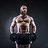 Strong bodybuilder with six pack, perfect abs, shoulders, biceps, triceps and chest. Power athletic bearded man in training pumping up muscles with dumbbell. 