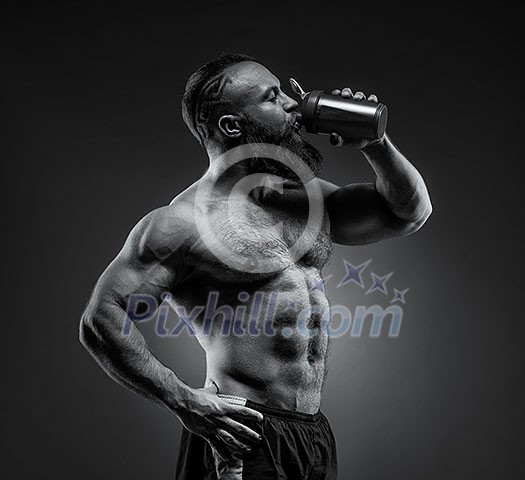 Bearded Man bodybuilder posing on gray background. Man is holding a shaker for drinks. Man drinking a protein shake, water, amino acids from the shaker. Sports nutrition, food additive. Bearded Man bodybuilder posing on gray background. Man is holding a shaker for drinks. Man drinking a protein shake, water, amino acids from the shaker. Sports nutrition, food additive.