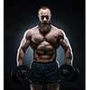 Bearded Muscular bodybuilder posing with heavy dumbbells on grunge background.