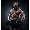 Strong bodybuilder with six pack, perfect abs, shoulders, biceps, triceps and chest. Power athletic bearded man in training pumping up muscles with dumbbell. 