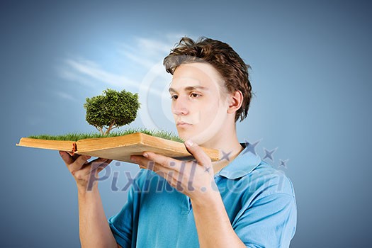 Young man in casual holding opened book with green tree Young man in casual holding opened book with green tree