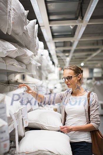 Pretty, young woman choosing the right pillow for her bed in a modern home furnishings store (color toned image; shallow DOF) Pretty, young woman choosing the right pillow for her bed in a modern home furnishings store (color toned image; shallow DOF)