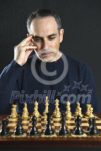 Man looking at wooden chess board thinking about first move Man looking at wooden chess board thinking about first move