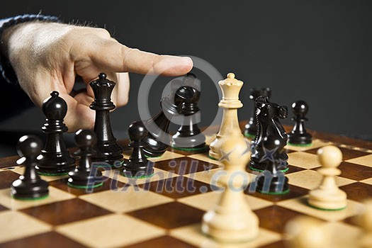 Finger pushing over King chess piece in defeat Finger pushing over King chess piece in defeat
