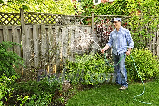 Man watering the garden with hose in backyard Man watering the garden with hose in backyard