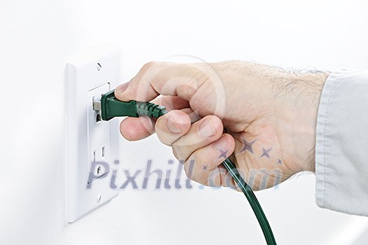 Hand inserting green electrical plug into outlet Hand inserting green electrical plug into outlet
