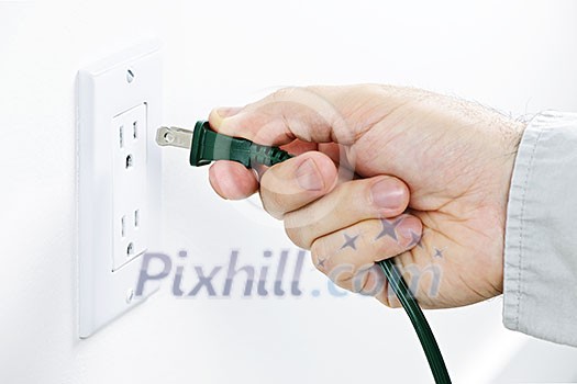Hand inserting green electrical plug into outlet Hand inserting green electrical plug into outlet