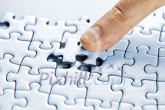Finger pushing missing puzzle piece into place Finger pushing missing puzzle piece into place
