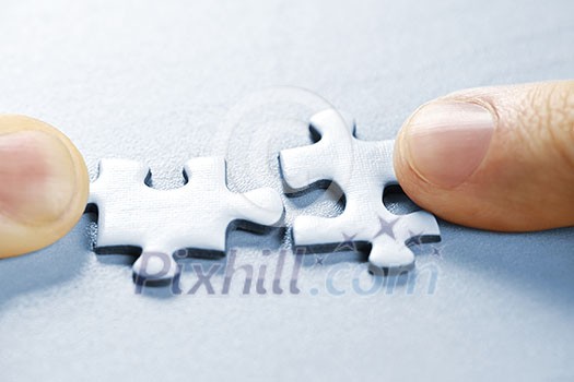 Fingers pushing two matching puzzle pieces together Fingers pushing two matching puzzle pieces together