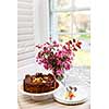 Round gourmet chocolate cake on table next to window with plates, cutlery, and pink spring bouquet