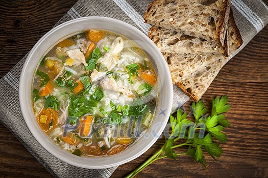 Chicken rice soup with vegetables in bowl and bread from above Chicken rice soup with vegetables in bowl and bread from above