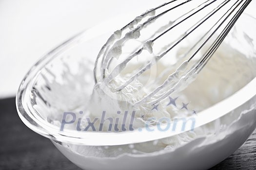 Closeup of metal whisk whipping cream in glass bowl Closeup of metal whisk whipping cream in glass bowl