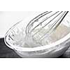 Closeup of metal whisk whipping cream in glass bowl