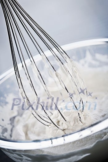 Closeup of metal whisk whipping cream in glass bowl Closeup of metal whisk whipping cream in glass bowl